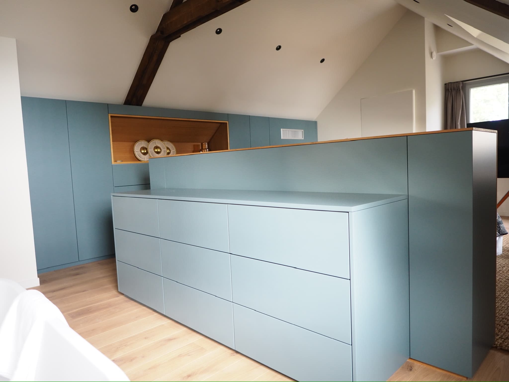 Commode en laque gris-bleu à l'arrière d'une tête de lit avec niche en chêne, chambre sous combles avec poutres apparentes, projet Quiberon A4 Créations