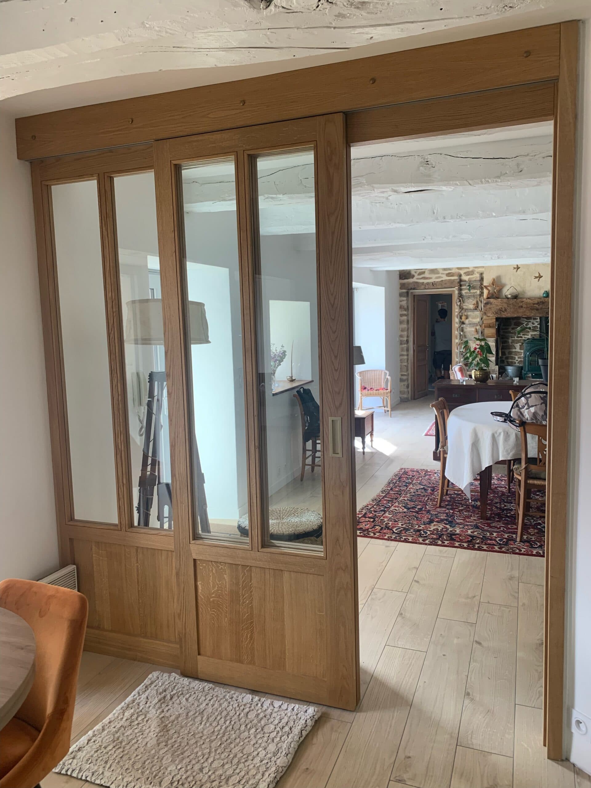 Verrière en chêne massif en cours de pose dans une maison avec pierre de taille et tapis, réalisation A4 Créations